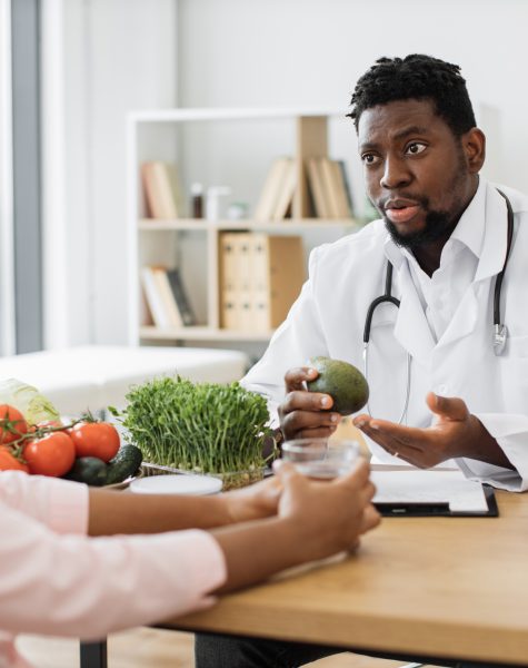 Focused middle-aged man reaching out microgreens in container while helping multicultural woman with health issues. Reliable expert in nutrition suggesting additional source of eating requirements.
